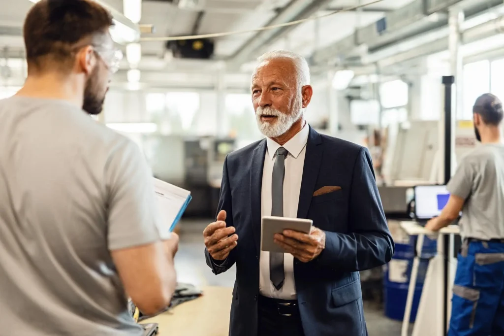 Vendor Onboarding. Senior company manager visiting employees in a factory plant and talking to one of the workers.